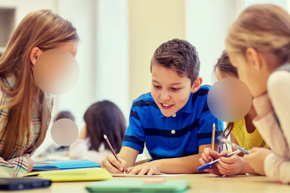 Dev at his desk with his classmates, classmates’ faces blurred